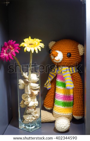 The knit brown teddy bear tied a scarf and placed in a box. Hand made crochet doll