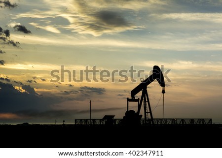 Cloudy sunset and silhouette of crude oil pumping unit in the oil field.
