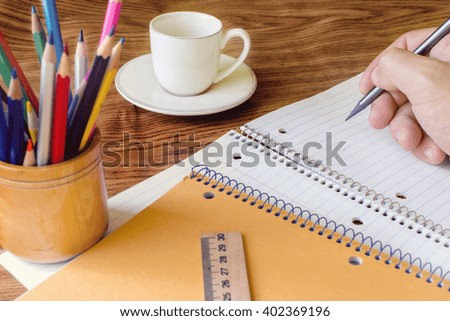 cup of coffee on a wooden table, notebook, pencil, wrist, pencils