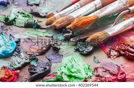used brushes in an artist's palette of colorful oil paint for drawing and painting