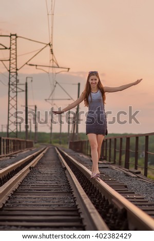happy girl walking on the rails with his arms raised towards the sunset