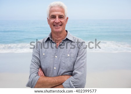 Portrait of senior man standing with arms crossed on beach on a sunny day