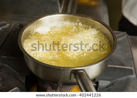 A pan of hot bubbling boiling oil in a silver pan on a hob. Royalty-Free Stock Photo #402441226