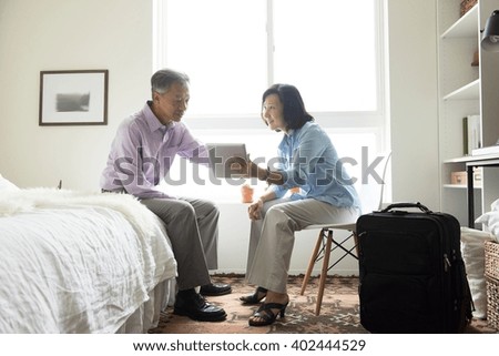 Mature couple sitting in hotel room with suitcase using digital tablet