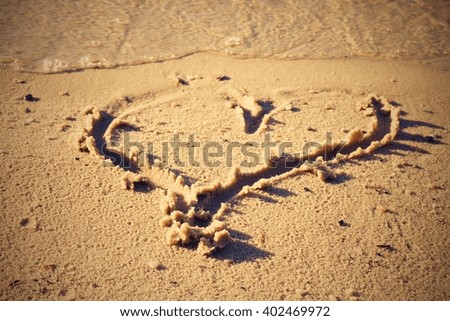 Holiday love. Lovely small heart sketched in salt  sand at beach. Evening warm colors of sunset mirror in water level.