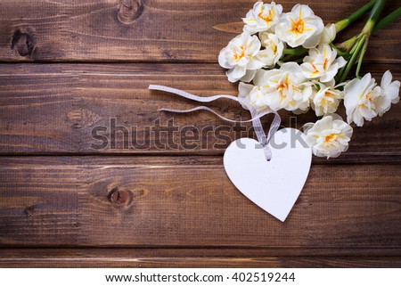 Spring yellow narcissus flowers and decorative  heart  on brown wooden background. Selective focus. Place for text.