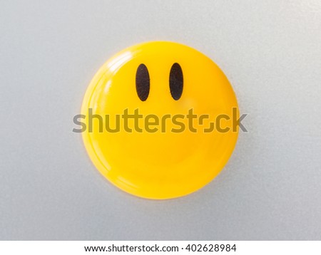Yellow magnet paper clip on gray refrigerator background, abstract background.