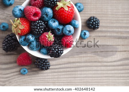 Mix of fresh berries in a basket on rustic wooden background. Close up, top view, high resolution product. Harvest Concept