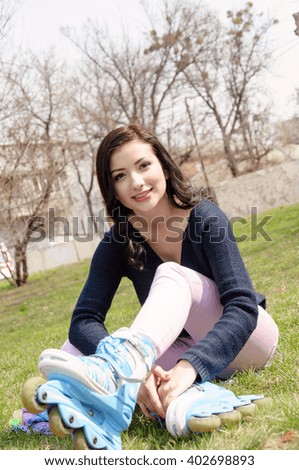 Girl wears roller skates sitting on the grass in the park. Concept: lifestyle, health, sport, activity.