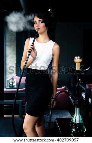 Young, beautiful woman smokes a hookah in cafe. It produces smoke from his mouth. Business style clothing. The pleasure of smoking. 