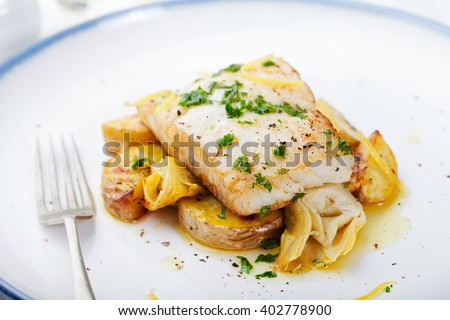 Roasted cod, codfish with baked potatoes and artichokes with lemon and herbs sauce on a white background