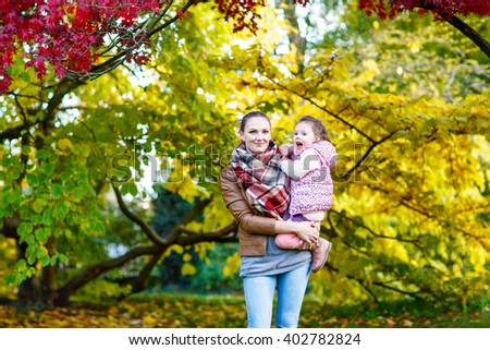 Young mother and her little daughter at beautiful autumn park. Kid girl and woman hugging and kissing. Family portrait outdoors.