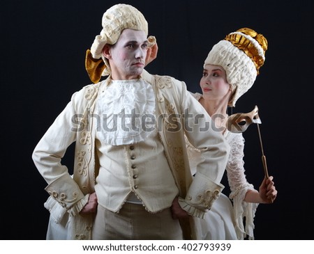 a man and a woman in period costume and wigs and holding a theatrical mask Royalty-Free Stock Photo #402793939