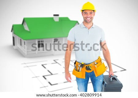 Portrait of smiling handyman holding toolbox against blue house behind an architectural plan