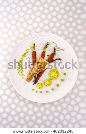 Fish dish in the restaurant - fried fish fillet with vegetables. Art food zender fried fillet with roasted baby carrots, puree and pistachio. Top view