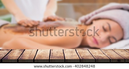 Attractive woman receiving chocolate back mask at spa center against wooden desk