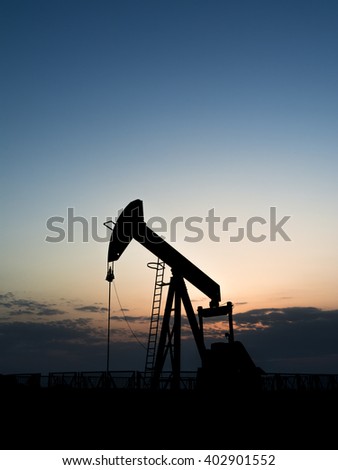 Sunset and silhouette of crude oil pump in the oil field.
