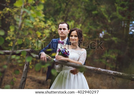 Beautiful pair of lovers newlyweds hugging in the woods.Hands holding a bouquet of lilac white lilac. Photo through the leaves of trees. He kisses her.