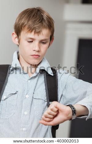 Schoolboy wearing a backpack checking his wristwatch for the time as he waits for his lift to school to ensure he is not late