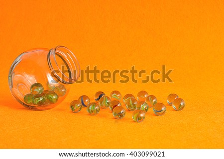 A collection of marbles in a glass jar displayed on an orange background