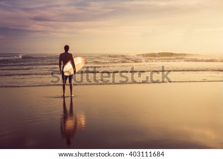 A man is standing with a surf in his hands on the sea shore.  Royalty-Free Stock Photo #403111684
