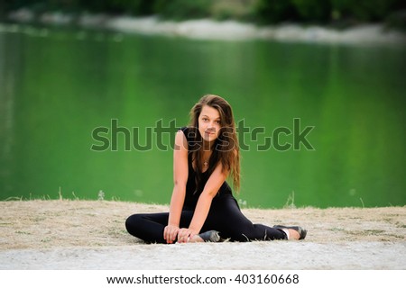 Young beautiful woman, ballerina dancer in black pointe shoes on green nature background near the lake. Cute girl with long hair posing outdoor. Sporty gymnast girl doing exercise in nature.