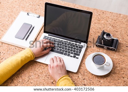 Businessman typing, coffee, notebook, smartphone and vintage camera around. Cork table, only hands seen. Concept of work.