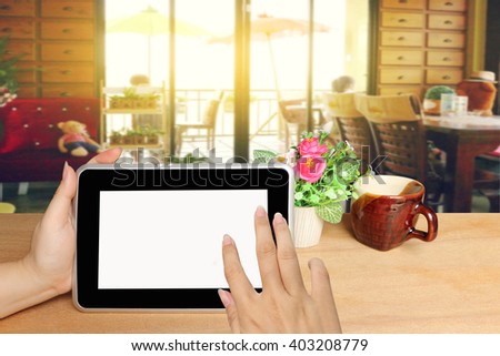 hand holding tablet on table with blur image of people in coffee shop background