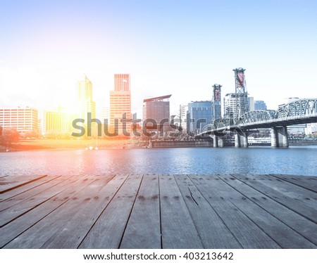 empty wood floor near steel bridge over water with cityscape and skyline of portland at sunrise