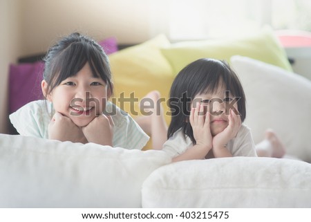 Happy sister and sad brother lying on white bed