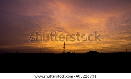 Cloudy Sunset and silhouette of drilling rig in the oil field
