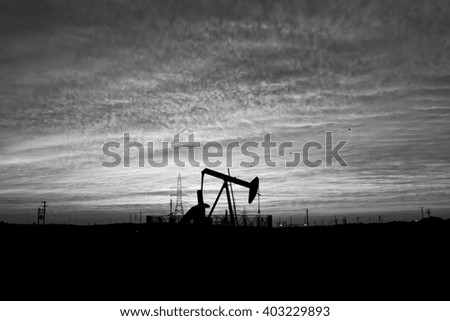 Cloudy sunset and silhouette of crude oil pump in oilfield - Black and white.
