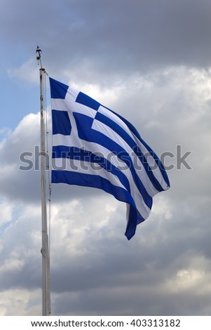 Greek flag on a flagpole against dark clouds