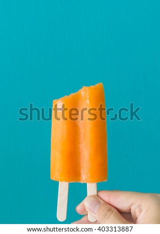 One hand holding bite orange ice cream in blue background