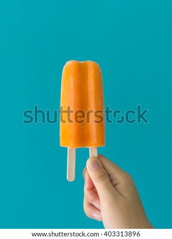 One hand holding orange ice cream in blue background