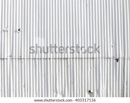 old decorative white wall painted metal gofrolist with dents, bumps and spots and peeling paint on an old fence