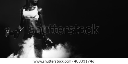 athletic woman. athletic girl with dumbbells. Studio photography. smoke effects. healthy athletic girl with massive dumbbells in his hands. working muscles. sport.dry working muscles. black and white/