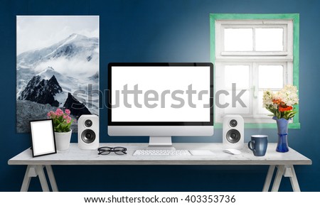 Computer display on office desk. Isolated, white screen for mockup. Creative modern desk with speakers, picture frame, glasses, keyboard, mouse, flowers, cup of coffee. Art canvas on blue wall. 