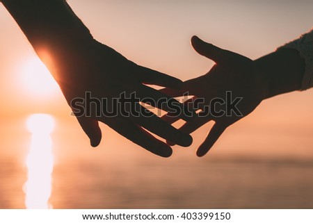 Couple hands reach silhouette on a sky and sea background. Evening photo. Royalty-Free Stock Photo #403399150
