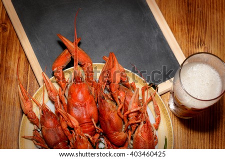 Boiled crawfish and glass of light beer and black chalkboard on a wooden table. Top view shot of fresh meals. Picture for bar or pub advertising, poster etc.