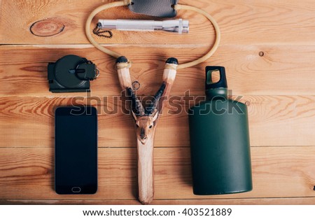 travel stuff - slingshot, bottle, compass, smart phone and light on wooden background