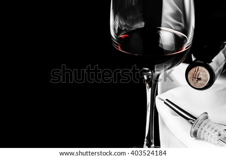 A glass of red wine, a bottle, white plate and napkin and a tube with dispenser on black background