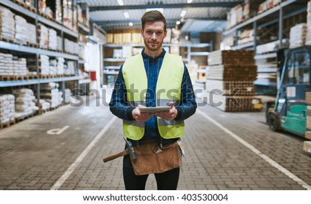 Young handyman or builder standing in the drive through in a hardware warehouse with a tablet in his hand looking at the camera Royalty-Free Stock Photo #403530004