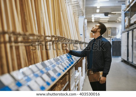 Carpenter selecting wood in a hardware store or warehouse standing looking at cut lengths on a rack, side view Royalty-Free Stock Photo #403530016