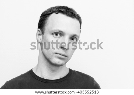 Young serious Caucasian man, close-up studio portrait over white wall background, black and white photo
