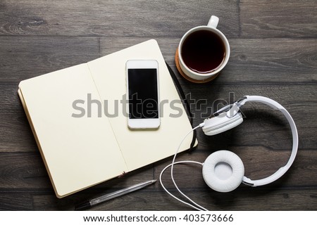  Top view of Smartphone with blank screen, earphones, notebook and coffee on wooden background
