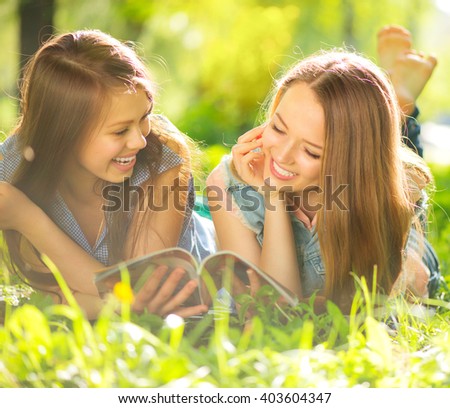 Beauty teen girls reading magazine and having fun outdoors. Beautiful joyful teenagers lying on spring grass, laughing and reading fashion magazine in spring park. Girlfriends outdoor. Friendship