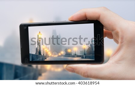 Tourist is photographing Charles Bridge in Prague with smartphone.