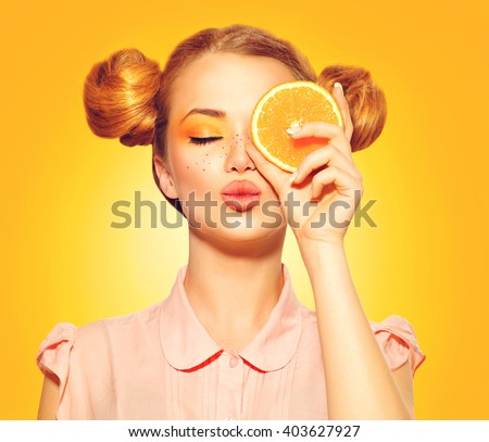Beauty Model Girl takes Juicy Oranges. Beautiful Joyful teen girl with freckles, funny red hairstyle and yellow makeup. Professional make up. Orange Slice  Royalty-Free Stock Photo #403627927