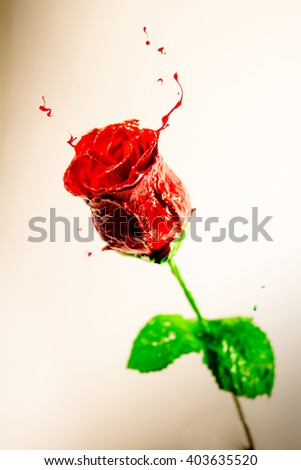 Red paint made beautiful rose with green leaves on orange background